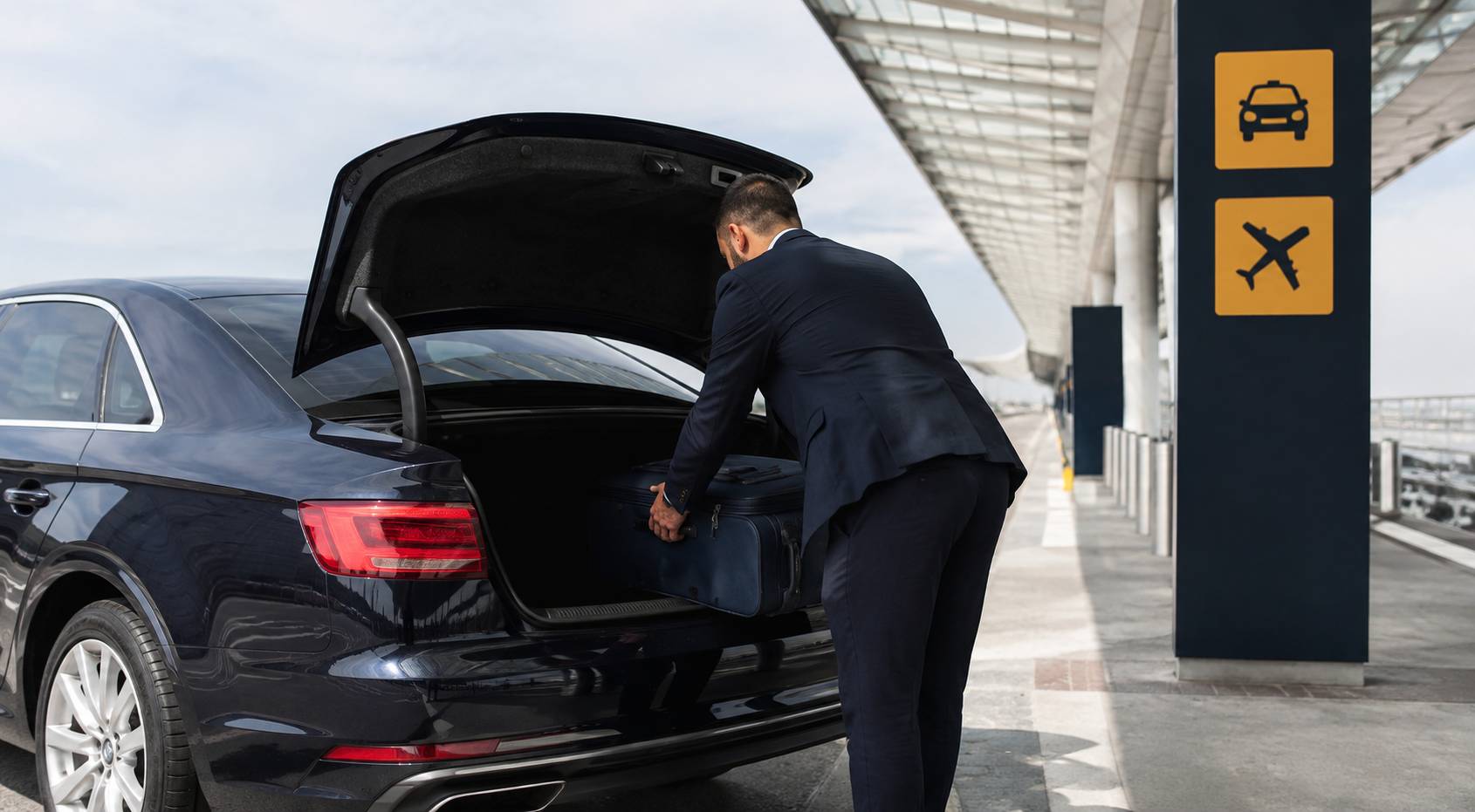 Chauffeur en costume chargeant des bagages dans le coffre d'une berline